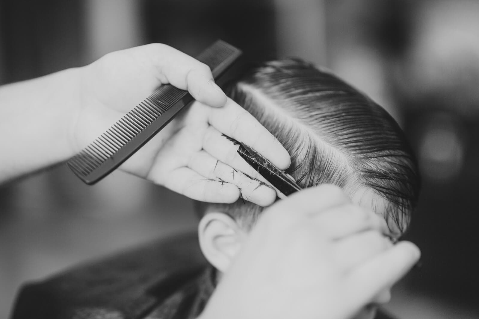 Barbier knipt een kapsel met zijscheiding met kam en schaar